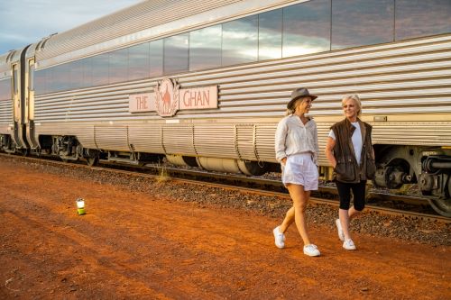 Two women walking by a carriage with a big Ghan logo on the side