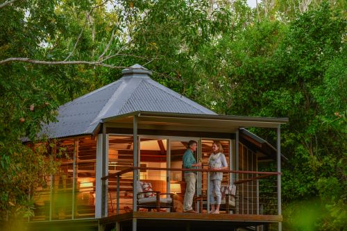 A couple standing and chatting on the balcony of their villa which is surrounded by green trees