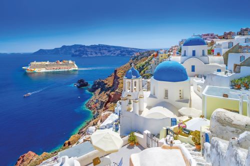 The famous blue-domed churches in Santorini overlooking the cliffside and Aegean Sea with the NCL vessel in the background at sea