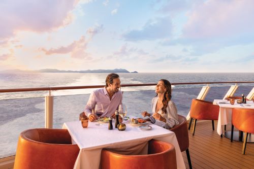 A couple enjoying dinner at the back of the vessel with a coastline in the distance. 
