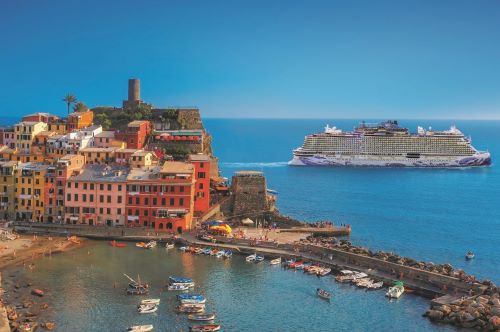Colourful coastal village of Cinque Terre with fishing boats at harbour and the grand NCL vessel in the background towards a bright blue sky