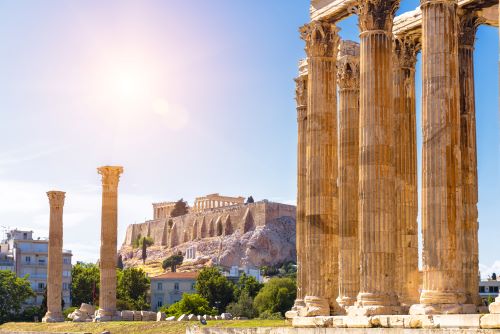 Majestic ancient columns stand before the Acropolis in Athens under the bright sun.