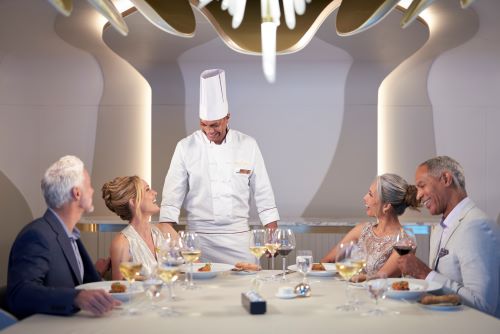 Two elegantly dressed couples enjoying dinner while smiling and chatting to the head chef. 