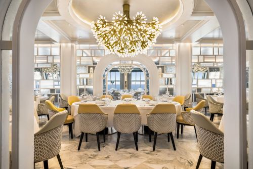 The Grand Dining Room aboard an Oceania vessel featuring big round tables set up for dining, huge chandeliers and interior that creates a contemporary ambiance