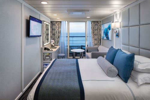The Veranda Stateroom with a king bed, lounge area and open balcony overlooking the ocean
