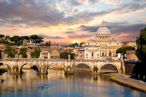 A serene view of St. Peter's Basilica and a historic bridge over the river at sunset in Rome.