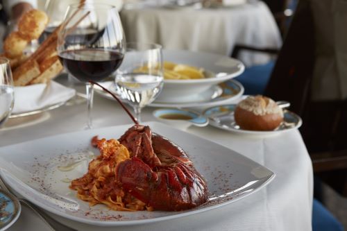 Close up of a lobster pasta dish deliciously arranged on the plate with a glass of wine and set dining table in the background