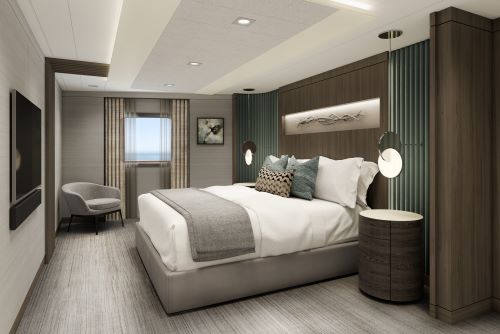 The interior of the Vista Suite Bedroom kept in shades of brown and grey featuring a bed, lounge chair and a window overlooking the sea