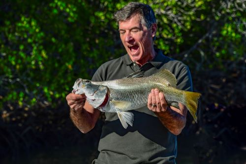 A very excited man holding a big Barramundi that he just caught