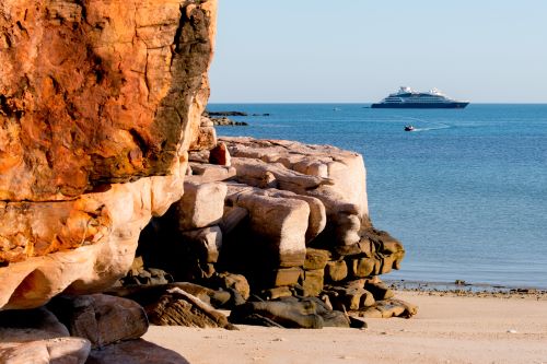 A red rock formation with the blue ocean and a cruise ship in the background