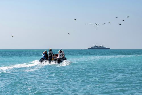 A small zodiac boat of tourists in the bright blue water making it's way to a cruise ship anchored in the ocean