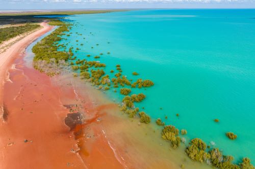 A red sandy beach meets the turquoise coastline
