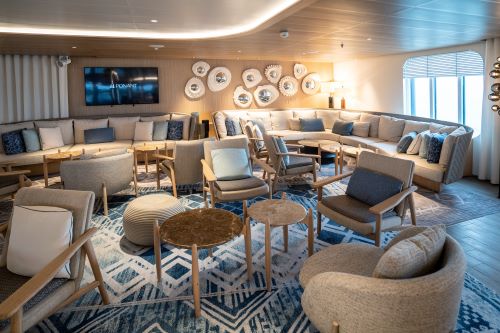 The main lounge onboard a cruise ship with small tables and lounge chairs and light interiors