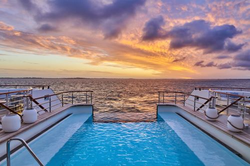The back deck of a cruise ship with an infinity pool and a sunset