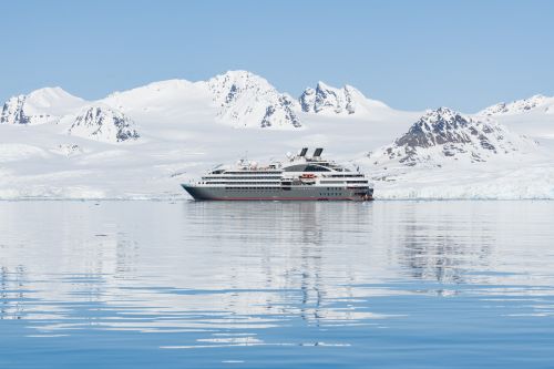 A small ship in the clear waters of the Arctic surrounded by ice bergs