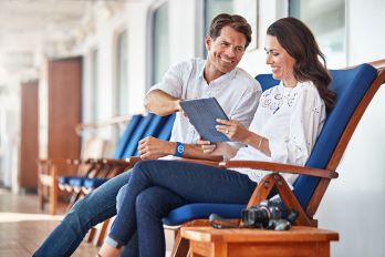 A couple smiling and sitting on deck in two of the sun lounges planning their day aboard Princess cruises