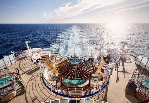 Looking down at the Pool deck of the Diamond Princess with three round whirlpools and sun lounges inviting to enjoy the sun and the wide ocean in the back of the ship