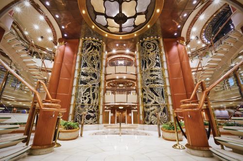 Atrium of a cruise ship with stairs on either side and lifts with brown interior 