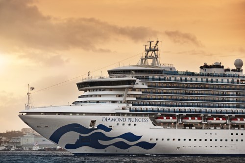 The Diamond Princess Cruise Ship docked in a port with passengers on the top deck waving to people in port