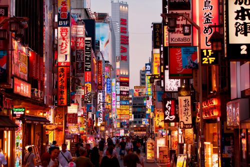 A shopping district in Japan with tourists walking through surrounded by large colourful billboards and signage 