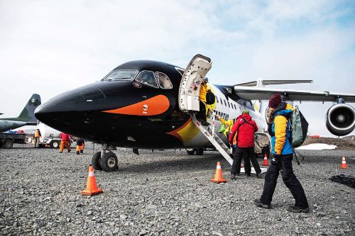 Passengers dressed in parkas and equipped with backpacks are boarding a charter plane