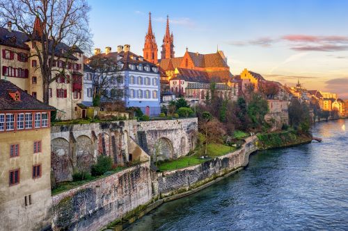 A charming riverside view of Basel, Switzerland, featuring historic architecture and a sunset glow.