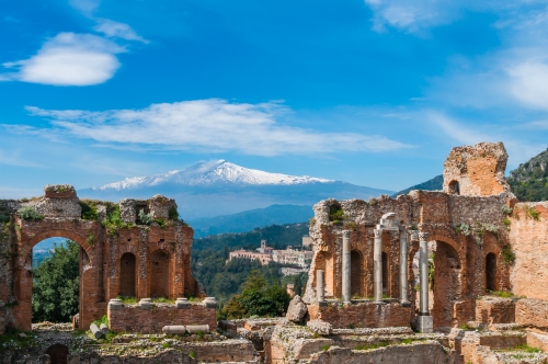 The ruins of an ancient, open-air amphitheatre with stunning views of Mount Etna in the background. 