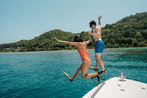 A couple jumping off a boat into clear blue water