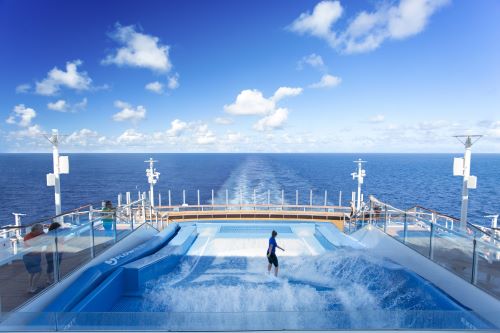 A person on an artificial wave rider onboard a cruise ship with the ocean in the background