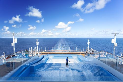 A person on an artificial wave rider onboard a cruise ship with the ocean in the background 