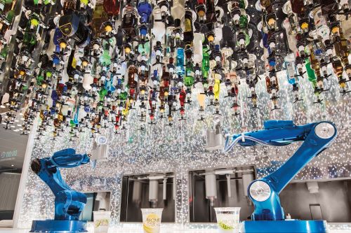 Lots of bottles hanning upside down from the ceiling and two robotic arms underneath designed to create cocktails. 