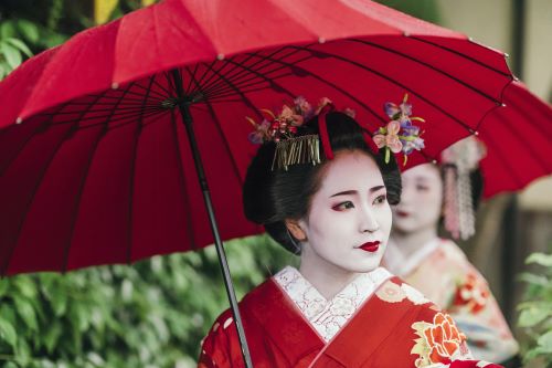 A beautiful Geisha Girl wearing a red kimono and holding a red parasol 