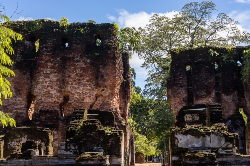 Ancient brick ruins with tall, weathered walls surrounded by lush green trees under a bright sky.