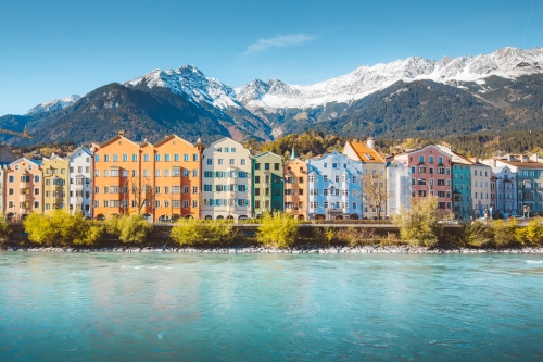 A row of colourful houses by the river with mountains covered by snow in the background