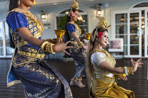 Three women dressed in traditional Cambodian dresses are performing a traditional dance to welcome passengers onboard