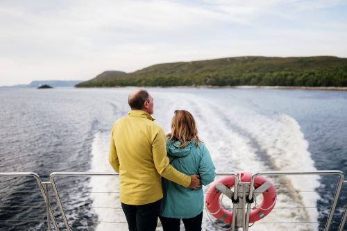 A couple standing at the back of a ship looking out to the land in the background