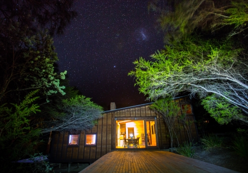 Modern lodge in the woods all lit up in front of a night sky full of stars