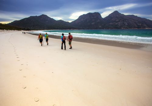 Hikers on a coastal walk on the beach enjoying picturesque views of Freycinet National Park