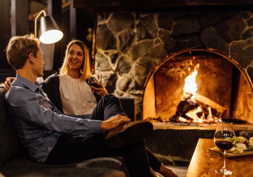 A couple chatting and drinking a red wine in front of a fireplace