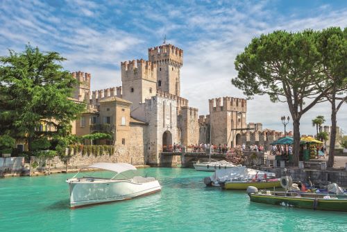 Some boats parked in a canal next to a big castle. 