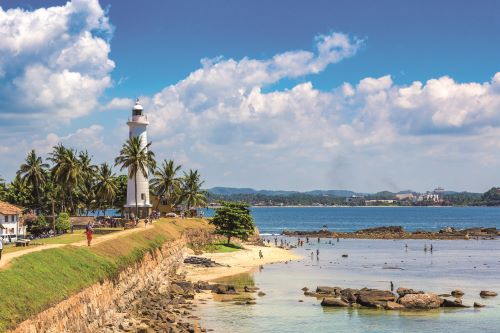 A lighthouse standing tall between palm trees overlooking a beach in Sri Lanka