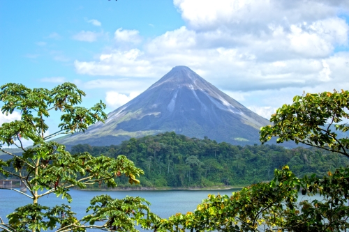Arenal Volcano towering above dense jungle with a lake and vibrant greenery in the foreground.