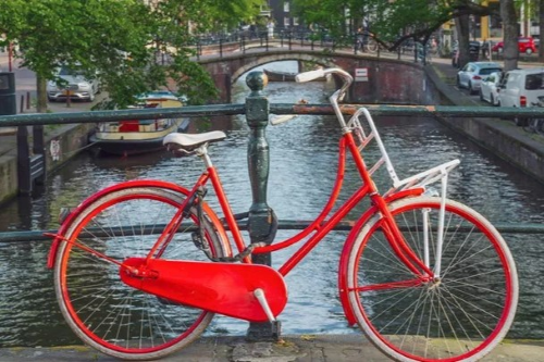 A red bicycle rests against a canal bridge in Amsterdam