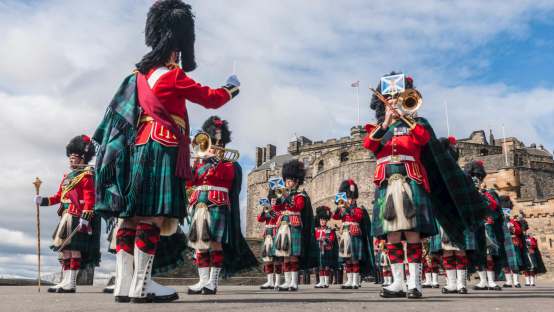 A marching band all dressed in traditional Scottish kilts performing the changing of the guard ceremony with the Edinburgh Castle in the background