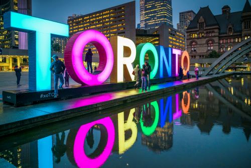 A big colourful lit up Toronto sign with people taking photos in front of it