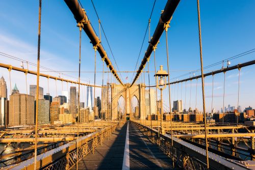 Photograph taken standing on the Brooklyn Bridge showcasing its symmetrical architecture with the New York skyline in the background