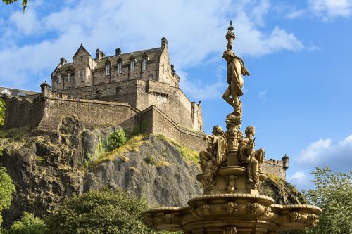 Low angle short of Edinburgh Castle and the Ross Fountain towards a blue sky with faint white clouds 