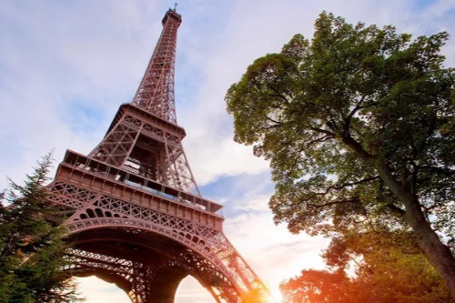 The Eiffel Tower rises against a glowing sunset, framed by trees in Paris