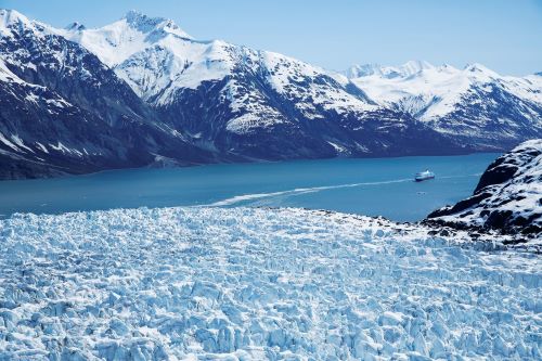 A cruise ship sailing through the blue waters of Glacier Bay which is surrounded by glaciers and snowy mountains 