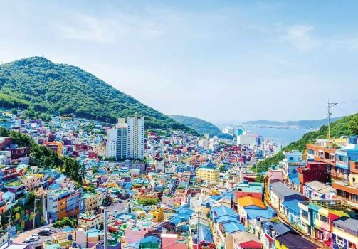 The busy village of Busan with its many colourful buildings and roofs sitting between green hills with the water in the background